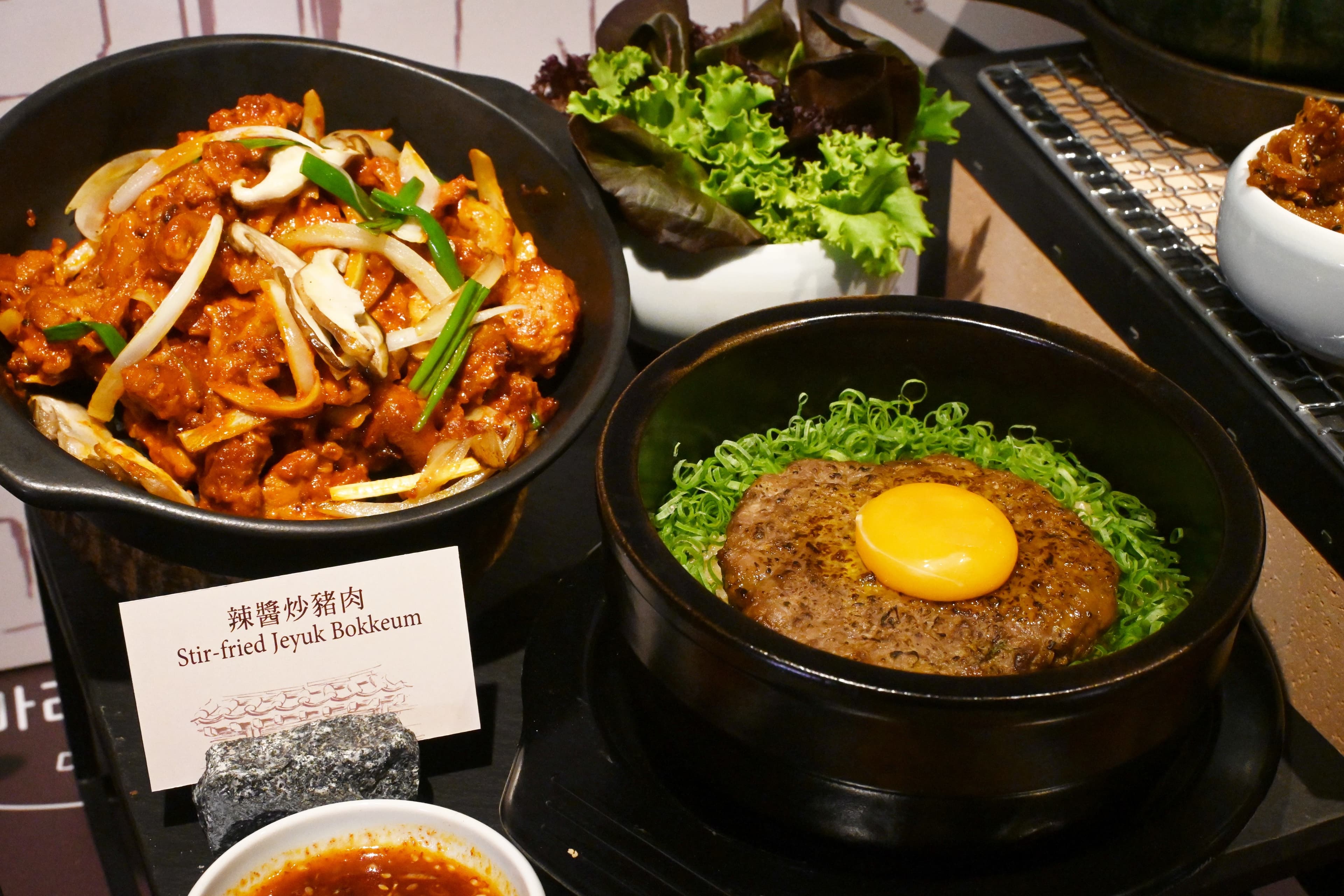 一樓azie推出4款韓式定食，每份皆搭配多道精緻韓式小菜，圖為「辣醬炒豬肉 」（左，980元／份）與「傳統韓式烤美國牛肉餅」（右，1,080元／份）。