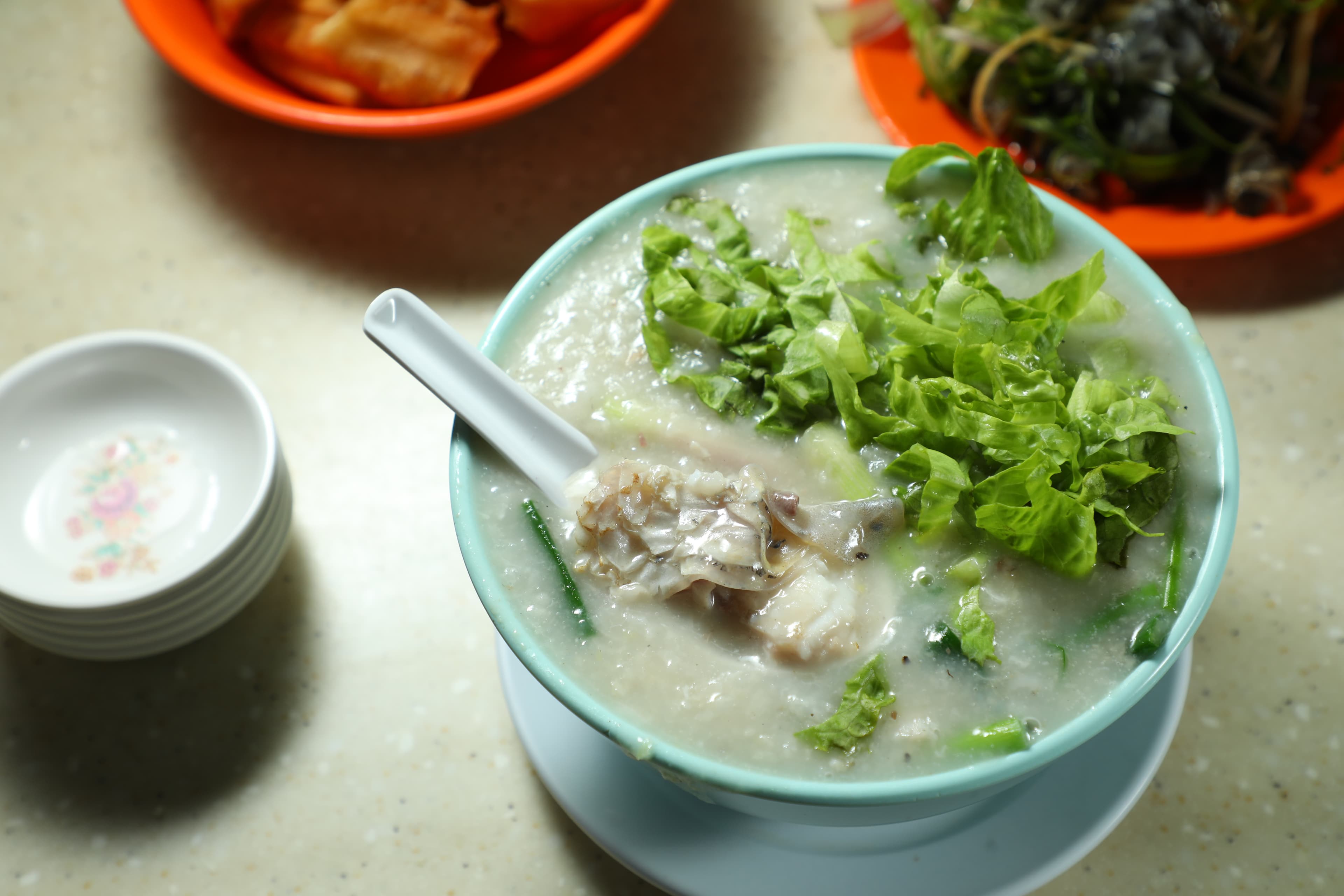 「魚腩粥」(前,港幣50元/碗)的粥面鋪滿生菜,能嘗到軟嫩魚肚,也可加點「油條」(後,港幣11元/份)來搭配。
