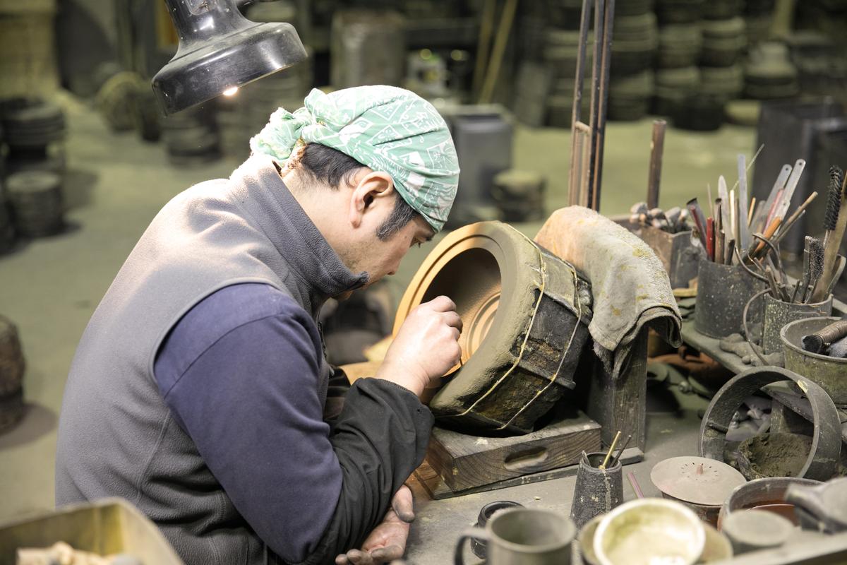 鑄鐵工匠單手托肘，專注地描繪花紋。